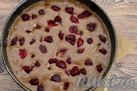 Дно разъёмной формы для выпечки диаметром 23 сантиметра застелить пергаментом. Растительным маслом смазать бока формы для выпечки и пергамент, застилающий дно формы. Вылить шоколадное тесто в форму. Поверх теста равномерно распределить вишню.