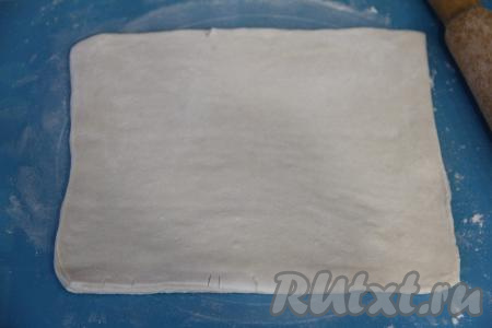 На присыпанной мукой поверхности размороженное слоёное тесто раскатать скалкой в прямоугольный пласт толщиной 3-4 миллиметра.