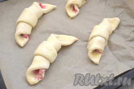 Сформированные круассаны выкладываем на расстоянии друг от друга на противень, застеленный пергаментом. Выкладываем круассаны так, чтобы "хвостик" (вершина треугольника) был внизу. В небольшой ёмкости соединяем яичный желток и молоко, взбиваем вилкой до однородности, получившейся смесью смазываем круассаны с малиной.