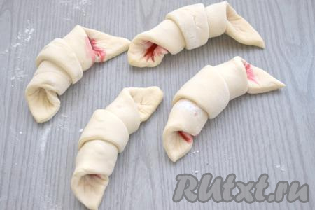 Начиная со стороны с надрезом, сворачиваем треугольник из слоёного теста в рулет. Таким образом формируем 4 заготовки круассана с малиной.