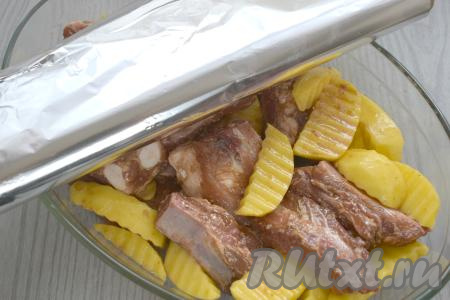 Через 10 минут перекладываем свиные рёбрышки с картошкой вместе с соевым соусом и маслом, в котором они мариновались, в жаропрочную форму для запекания. Форму накрываем плотно фольгой и отправляем в духовку, заранее разогретую до 180 градусов.