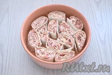 Рулет с фаршем разрезаем на равные кусочки шириной примерно 2,5-3 сантиметра. В форму для запекания, смазанную растительным маслом, ставим на срез кусочки рулета из лаваша - это и будут заготовки ленивых пельменей. 