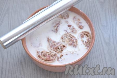 В отдельной ёмкости смешиваем сметану и 400 миллилитров воды комнатной температуры, солим, приправляем специями (я всыпала немного чёрного молотого перца), тщательно перемешиваем получившийся сметанный соус. Вливаем соус из сметану в форму с ленивыми пельменями. Соус должен практически полностью покрыть рулетики из лаваша. Форму накрываем фольгой.