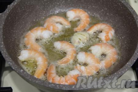 Выложить в разогретое чесночное масло очищенные креветки и обжарить на среднем огне по 1 минуте с каждой стороны. Переложить жареные креветки со сковороды на тарелку, дать немного остыть.