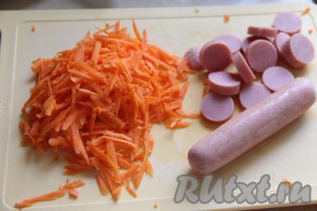 Пока лук обжаривается, морковь натереть на крупной тёрке. Сосиски очистить от слюды, а затем нарезать на кружочки.