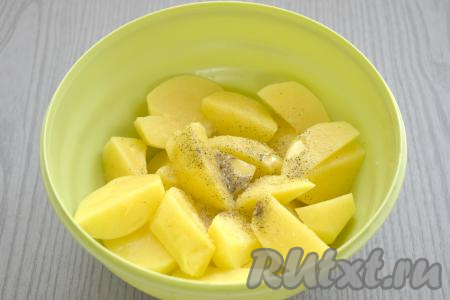 По прошествии часа очищаем картофель, нарезаем его на средние ломтики, перекладываем в отдельную миску. Немного солим картошку, приправляем специями (я добавила чёрный молотый перец), вливаем растительное масло. Тщательно перемешиваем, распределяя масло и специи по всему картофелю.