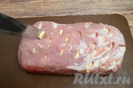 В мякоти свинины острым широким ножом сделать очень глубокие надрезы. В каждый надрез вставить по пластине чеснока.