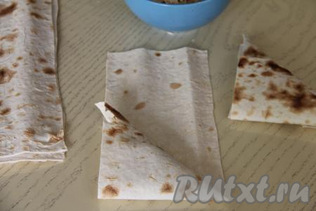 Завернуть угол полоски из лаваша на начинку по диагонали, формируя треугольник. Далее, продолжая заворачивать лаваш с начинкой в виде треугольника, сформировать треугольную самсу.