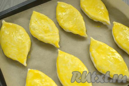 Аналогично лепим оставшиеся 7 пирожков. На противень, застеленный пергаментом, выкладываем пирожки швом вниз. Яичный желток в небольшой ёмкости взбиваем вилкой до однородности. Поверхность пирожков смазываем взбитым желтком.