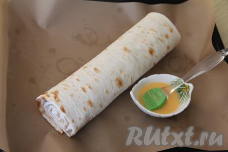 В небольшой пиале взбить вилкой желток. Переложить рулет на противень, застеленный ковриком (или пергаментом) для выпечки. С помощью силиконовой кисточки смазать желтком поверхность рулета из лаваша, по желанию, присыпать кунжутом.