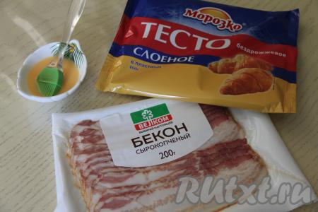 Подготовить продукты для приготовления рулетиков с беконом из слоёного теста. Разморозить слоёное тесто (подойдёт как дрожжевое, так и бездрожжевое покупное слоёное тесто) при комнатной температуре. Бекон я взяла сырокопчёный, уже нарезанный на полоски.