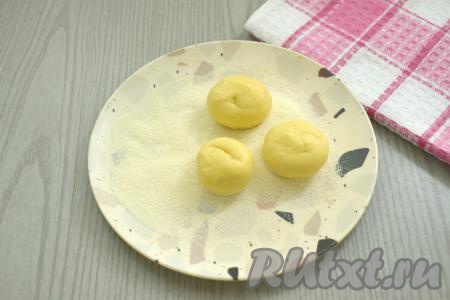 Затем делим тесто на 24 одинаковых кусочка. Из кусочков теста скатываем шарики размером немного больше грецкого ореха. На тарелку всыпаем 3 столовых ложки манки. Шарики из теста одной стороной опускаем в тарелку с манкой.