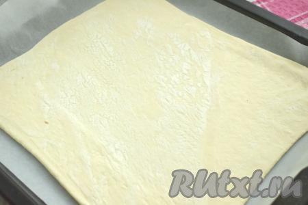 У меня слоёное тесто было в 2 пластах. Вначале один пласт размороженного слоёного теста выкладываем на стол, присыпанный мукой, раскатываем в квадрат со стороной 26 сантиметров. Сразу раскатанный пласт слоёного теста помещаем на противень, застеленный листом для выпечки (или пергаментом).