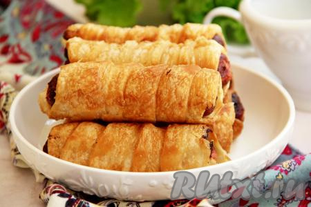 Аппетитные сосиски в слоёном бездрожжевом тесте, жаренные на сковороде, можно есть и тёплыми, и остывшими. Их можно подать к чаю, брать с собой на работу в качестве перекуса или давать детям в школу.