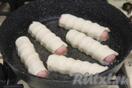 В сковороду влить достаточно много растительного масла, хорошо его разогреть. Выложить сосиски в тесте в сковороду.