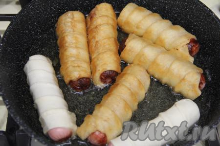 Готовить на среднем огне, периодически переворачивая, чтобы сосиски в тесте прожарились со всех сторон.