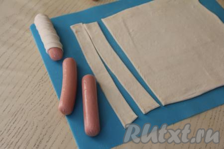 Сосиски очистить от слюды. Нарезать тесто на полоски шириной примерно 1,5 сантиметра.
