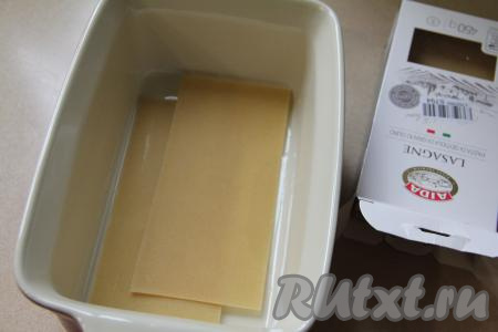 Теперь можно приступать к формированию лазаньи. Сыр натереть на крупной тёрке. По желанию, форму, в которой вы будете формировать лазанью, можно смазать растительным маслом. На дно достаточно глубокой формы для запекания (я использовала форму размером 23 сантиметра на 15 сантиметров) выложить пару листов для лазаньи. Я листы лазаньи перед выкладыванием в форму не отваривала. В процессе запекания они хорошо пропитываются соусом из рикотты и мясными соками, поэтому успевают полностью приготовиться и становятся мягкими, но не переваренными, хорошо держат формы. Но советую ознакомиться с инструкцией на упаковке листов лазаньи, которые вы используете. Некоторые производители советуют предварительно отваривать листы.&nbsp;