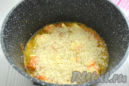 Пока тушится мясо, хорошо промываем рис проточной водой, даём лишней воде стечь. Головку чеснока очищать не нужно, но её нужно хорошо ополоснуть водой. Рис достаточно ровным слоем выкладываем поверх курицы, протушившейся с овощами, по вкусу солим.