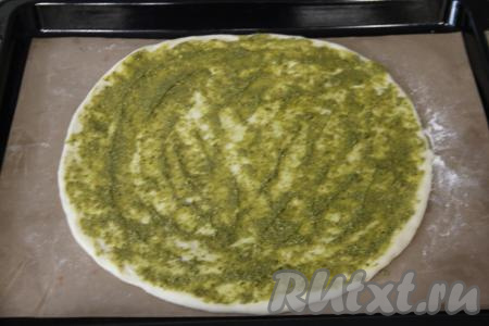 На тефлоновом коврике (или на бумаге) для выпечки раскатать дрожжевое тесто в круг диаметром 28 сантиметров. Коврик (или бумагу) вместе с раскатанным тестом аккуратно переложить на противень. Смазать раскатанное тесто соусом песто. 1 чайную ложку песто я оставила для украшения пиццы.&nbsp;