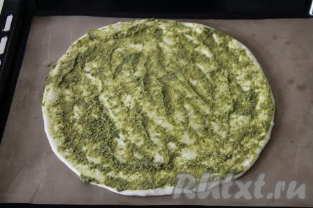 Переложить тесто вместе с бумагой (или ковриком), на которой вы его раскатывали, на противень. Раскатанное тесто смазать соусом песто.