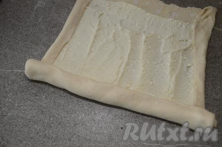 Немного подвернуть длинные стороны прямоугольника на начинку и, начиная с короткой стороны, свернуть тесто в плотный рулет.