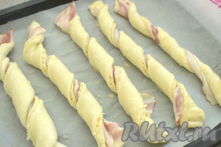 Сформированные палочки с беконом и сыром выкладываем на противень, застеленный пергаментом. Сверху смазываем палочки оставшимся взбитым яйцом.