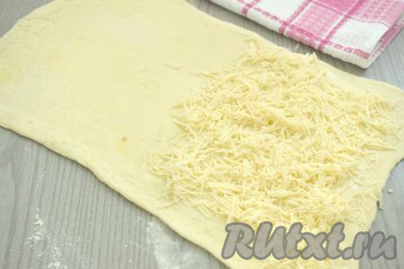 Раскатанное тесто визуально делим на 2 половины. Сыр натираем на крупной тёрке и выкладываем его на одну половину теста, отступая от краёв теста по 1-1,5 сантиметра.