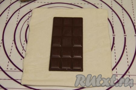 На слегка присыпанной мукой поверхности раскатать размороженный пласт теста до толщины примерно 3 миллиметра. На середину получившегося пласта выложить плитку шоколада.