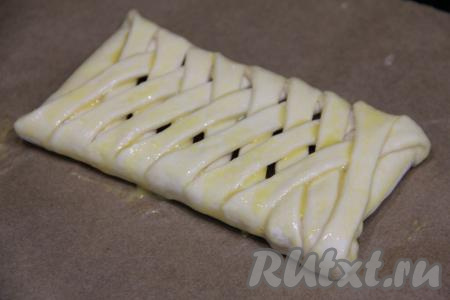 Сформированную косичку с шоколадом переложить на противень, застеленный пергаментом. В небольшой ёмкости взбить вилкой яичный желток, а затем смазать им верх косички из слоёного теста.