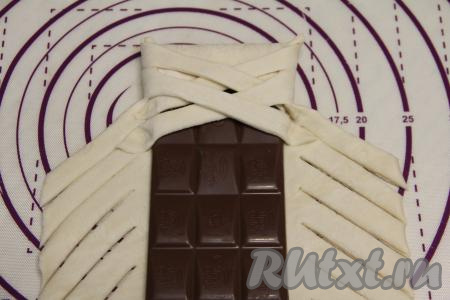 Затем поверх шоколада, начиная с подвёрнутого края, приступить к заворачиванию полосок теста с двух сторон внахлёст, формируя косичку. Край каждой завёрнутой полоски нужно крепить к тесту, как на фото.