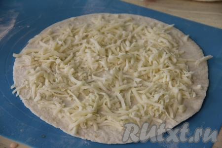 Взять первую тортилью, равномерно выложить на неё половину натёртого сыра, немного отступая от краёв лепёшки.