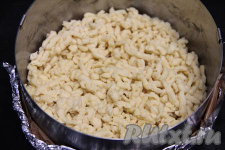 Достать одну часть теста из морозилки, натереть на крупной тёрке. Равномерно выложить натёртое тесто на дно разъёмной формы для выпечки диаметром 20 сантиметров. В качестве формы я использовала разъёмное кулинарное кольцо диаметром 20 сантиметров, сформировав дно из пергамента и фольги, сложенных в несколько слоёв.