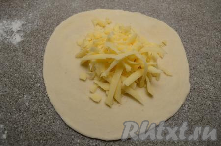 Сыр натереть на крупной тёрке, разделить его на 4 равных части (по количеству рулетиков из слоёного теста). Одну часть сыра выложить в центр раскатанного круга из теста.