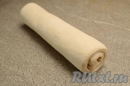 На слегка присыпанной мукой поверхности размороженный пласт слоёного теста, не раскатывая, свернуть в рулет.