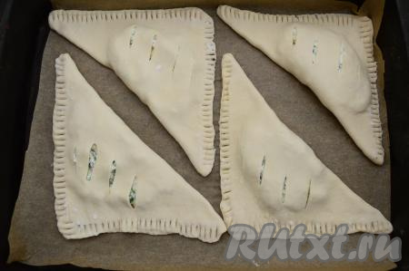 Сформированную заготовку слойки с творогом и зеленью выложить на противень, застеленный пергаментом. Аналогично сформировать ещё 3 заготовки слоек, выложить их на застеленный противень, размещая на небольшом расстоянии друг от друга.