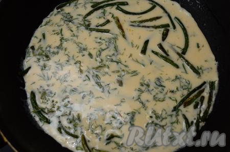 В сковороду с чесночными стрелками, обжаренными до готовности, влить яично-молочную смесь, перемешать. Накрыть сковороду крышкой, сделать огонь ниже среднего.