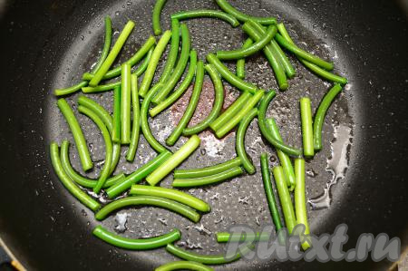 На сковороду влить 2 столовых ложки растительного масла, немного прогреть, выложить стрелки чеснока. Жарить чесночные стрелки в течение 5 минут на среднем огне, при этом каждую минуту их следует перемешивать.