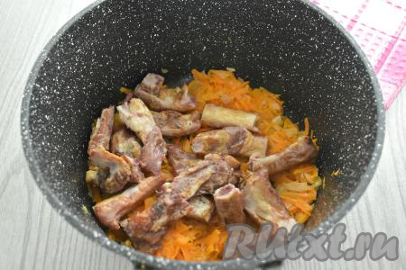 Крупные копчёные рёбрышки разрубаем на части. Добавляем копчёные рёбра к обжаренным луку и моркови, перемешиваем, готовим 3 минуты, время от времени помешивая.