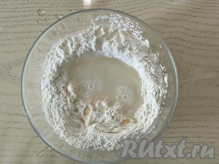 Влить воду комнатной температуры, перемешивать тесто сначала ложкой. В процессе перемешивания оно начнёт собираться в ком, после этого начать вымешивать его руками.