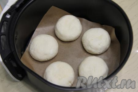 На отдельную тарелку насыпать 2 столовых ложки рисовой муки. Руками, смоченный водой, из каждой части творожной массы сформировать округлый сырник, затем обвалять его со всех сторон в рисовой муке. Дно чаши аэрогриля застелить пергаментом, выложить сформированные сырники.