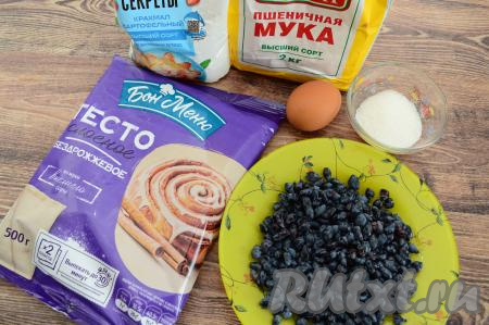 Подготовить продукты для приготовления слоек с жимолостью. Слоёное тесто для этих слоек можно купить дрожжевое или бездрожжевое. Заранее достать слоёное тесто из морозилки и оставить его размораживаться при комнатной температуре. Жимолость можно взять как свежую, так и замороженную. Свежую жимолость нужно будет перебрать, убирая листочки и сор, промыть ягоды проточной водой, после этого разложить их на бумажном полотенце, чтобы они немного обсохли. Замороженную жимолость, если на ней нет большого количества льда, можно не размораживать.