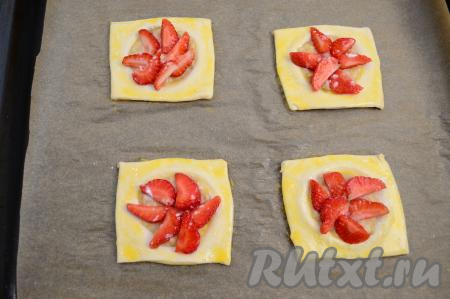 Вилкой в небольшой ёмкости взболтать яичный желток до однородности. При помощи кулинарной кисти&nbsp;получившейся яичной смесью смазать тесто слоек. Каждую слойку (и клубнику, и тесто) присыпать 0,5 чайной ложки сахара.&nbsp;