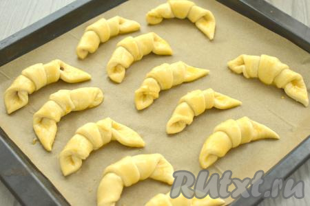 Рогалики с изюмом, сформированные из слоёного теста, выкладываем на небольшом расстоянии друг от друга на противень, застеленный пергаментом. В небольшой ёмкости взбиваем вилкой до однородности яичный желток. С помощью силиконовой кисточки смазываем поверхность рогаликов взбитым желтком.