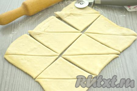Размороженный пласт слоёного теста выкладываем на стол, присыпанный мукой. Раскатываем тесто в прямоугольник (у меня получился прямоугольник со сторонами 30 сантиметров на 20 сантиметров). Разрезаем получившийся прямоугольник на 6 одинаковых квадратов. Затем каждый квадрат разрезаем по диагонали. В итоге у нас получатся 12 треугольников.