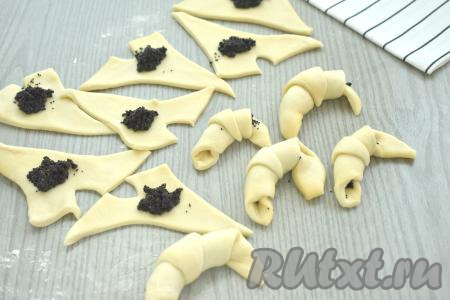 Углы короткой стороны треугольника разводим в стороны. Возле разрезов, немного отступив от краёв теста, выкладываем чуть больше половины чайной ложки начинки из мака. Сворачиваем каждый треугольник, начиная со стороны с маком, в рогалик.