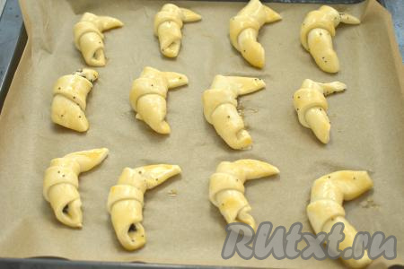 Сформированные рогалики с маком выкладываем на небольшом расстоянии друг от друга на противень, застеленный пергаментом. Вилкой в небольшой ёмкости взбиваем яичный желток до однородности. Взбитым желтком с помощью силиконовой кисти смазываем поверхность каждого рогалика.