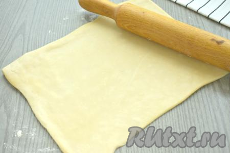 Посыпаем стол немного мукой, выкладываем разморозившееся тесто, раскатываем его скалкой в прямоугольный пласт размером 30 сантиметров на 20 сантиметров.