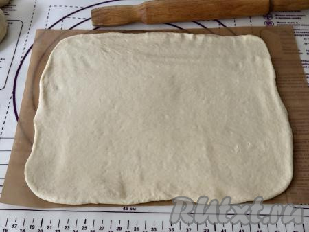 Большую часть теста на присыпанной мукой поверхности раскатать в прямоугольный пласт размером примерно 45 сантиметров на 30 сантиметров, переложить на коврик (или на бумагу) для выпечки.