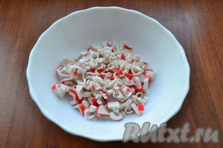 Яйца сварить вкрутую (в течение 10 минут с момента закипания воды), затем полностью остудить их и очистить. Крабовые палочки разморозить при комнатной температуре, вынуть из упаковки. Нарезать крабовые палочки кружочками в глубокую тарелку.